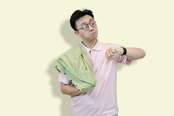Young Asian man wearing glasses and a polo shirt, holding a jacket, looking at his wristwatch with...