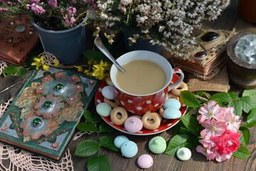 Cozy still life with cup of tea with milk, decorated book and sweets with flowers on the table....