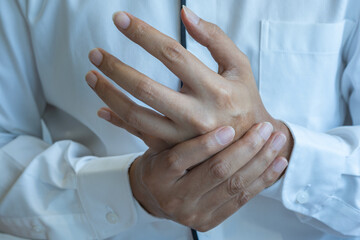 An Asian man clutches their left hand, indicating possible joint pain or musculoskeletal...