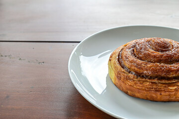 Half view of one sweet Cinnamon roll dessert on white plate. Isolated on wooden table background. copy space, empty, free, negative. close up.