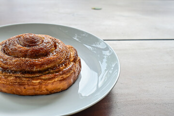 Half view of one sweet Cinnamon roll dessert on white plate. Isolated on wooden table background. copy space, empty, free, negative. close up.