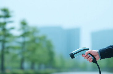 Electric vehicle charger hand technology outdoor green trees modern buildings urban eco friendly