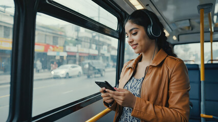 Smiling woman with headphones using smartphone on bus wearing tan jacket