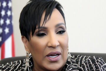 Confident Black entrepreneur meets the camera in a stylish office, US flag draped behind, her steady gaze radiates leadership and ambition.
