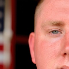 Focused male medic grips lifesaving gear in ambulance bay, soft US flag backdrop highlights urgent dedication.