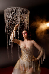 Caucasian female artist in golden Victorian-inspired corset costume, front view, dark background. Ideal for retro, Edwardian, cabaret, or theatrical performance themes.