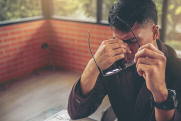 Tired businessman taking off glasses with eye pain and headache during working in office. Selected focus