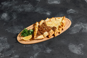 Turkish pide mix with cheese and meat, bright mood, overhead composition on dark textured surface