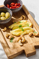 Halloumi slices with green olives and sundried tomatoes, bright lighting, overhead wooden board composition