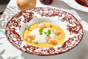Pumpkin soup with shrimp in sunlight, ornate floral plate flatlay