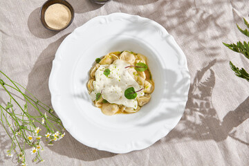 Pelmeni with cheese espuma in bright rustic lighting, overhead composition on linen tablecloth