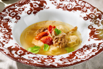 Broth with pelmeni and cheek meat in bright lighting, overhead composition