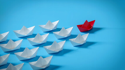 Obraz premium One red paper boat leads a fleet of white paper boats in formation against a bright blue background