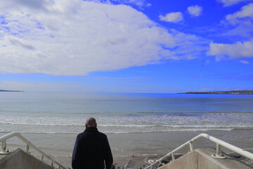 Fototapeta premium Man standing on rocky shoreline Lahinch Beach, Liscannor Bay, County Clare, Ireland on a bright summer morning. Scenic Atlantic coast, blue sky, peaceful seaside, Irish travel and lifestyle concept.