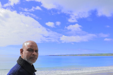 Man standing on rocky shoreline Lahinch Beach, Liscannor Bay, County Clare, Ireland on a bright...