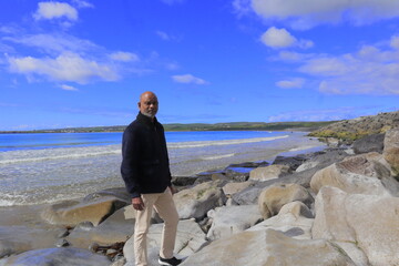 Man standing on rocky shoreline Lahinch Beach, Liscannor Bay, County Clare, Ireland on a bright...