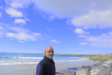 Man standing on rocky shoreline Lahinch Beach, Liscannor Bay, County Clare, Ireland on a bright...