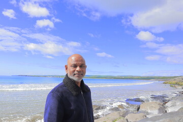 Man standing on rocky shoreline Lahinch Beach, Liscannor Bay, County Clare, Ireland on a bright...
