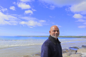 Man standing on rocky shoreline Lahinch Beach, Liscannor Bay, County Clare, Ireland on a bright...
