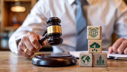 Judge holding a gavel near wooden blocks with environmental symbols representing sustainability and legal decisions