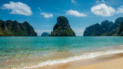 Fototapeta premium Idyllic tropical beach with turquoise water white sand and lush green limestone karsts under a bright blue sky with clouds