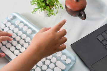 Child's hands typing on a modern retro-style keyboard. Creative tech scene with vintage elements and a clean, minimalist workspace