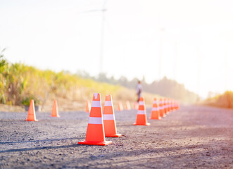 Traffic cones lined up on a rural road under bright sunlight, symbolizing safety, caution, and...