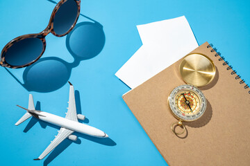 Airplane, compass, sunglasses, and notebook on a blue background. Mockup or Copy space. Travel...