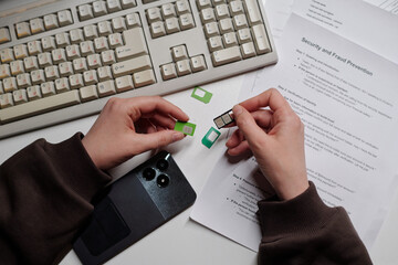 Woman holding SIM card and adapter near smartphone and documents, preparing device at desk,...