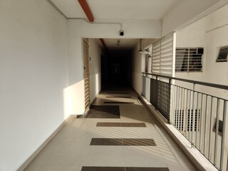The exterior walkway of a high-rise residential building at dusk. There is a dark alley in the...