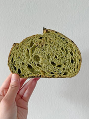 Matcha bread slice held against white wall.