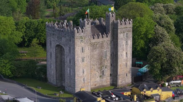 Bunratty Castle In County Clare, Ireland - Stone Fortress With Battlements And Irish Flags Surrounded By Lush Greenery. static aerial shot