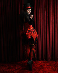 Burlesque circus performer, female model, in red corset and striped stockings in jester clown...