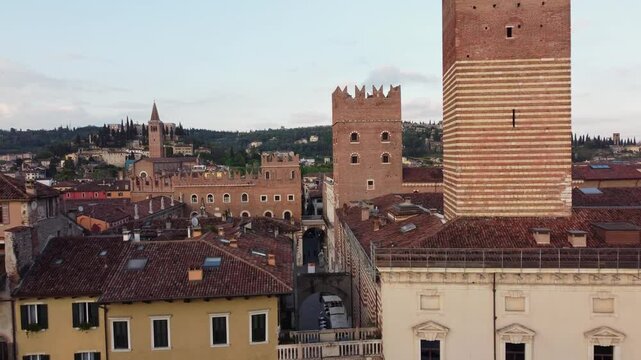 Drone frames Verona&rsquo;s historic center with Torre dei Lamberti (striped), Palazzo del Podest&agrave;, Arco della Costa, and San Zeno Basilica on the hill, real time, golden hour, aerial wide view