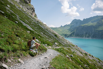 Hiker resting on mountain trail overlooking turquoise lake and peaks