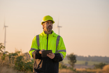 Engineer man working with tablet at windmill farm Generating electricity clean energy. Wind turbine...