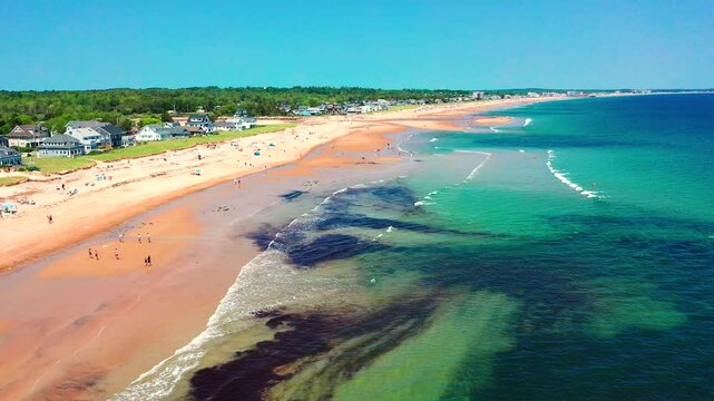 Aerial drone video of Saco, Maine coastline in summer. Tourists fill the sandy beach near vacation houses, waves hit shore, families relax. A beautiful East Coast getaway in full peak-season swing.