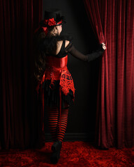 Burlesque circus performer, female model, in red corset and striped stockings in jester clown...
