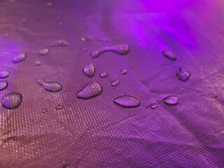 Water droplets on a textured, purple-lit surface.