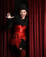 Burlesque circus performer, female model, in red corset and striped stockings in jester clown...