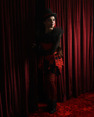Burlesque circus performer, female model, in red corset and striped stockings in jester clown...