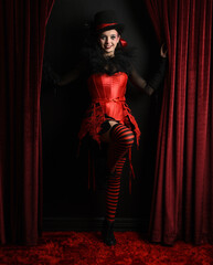 Burlesque circus performer, female model, in red corset and striped stockings in jester clown...
