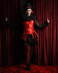 Burlesque circus performer, female model, in red corset and striped stockings in jester clown...