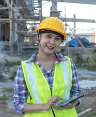 Vertical Asian female construction worker with helmet holding tablet working in construction site