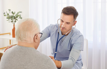 Young male physician doctor with stethoscope examining senior man's lungs, breathing and heartbeat....