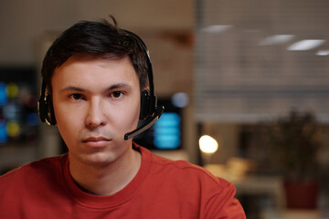 Portrait of young adult Asian man wearing headset staring directly at camera working in scam call...