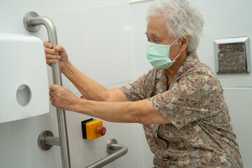 Asian elderly woman patient use toilet support rail in bathroom.