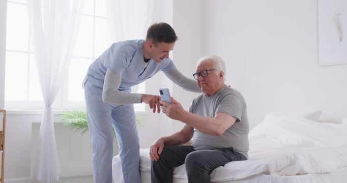Positive doctor or caregiver assists an elderly man in using a phone and online technology at a nursing home. Guidance in navigating the internet and digital devices for the elderly. - Powered by Adobe