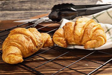 Freshly baked croissants on a cooling tray with tongs and a napkin on the table