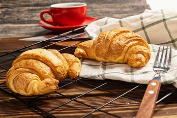 Freshly baked croissant and a cup of coffee with a fork and a napkin on a cooling tray on the table
